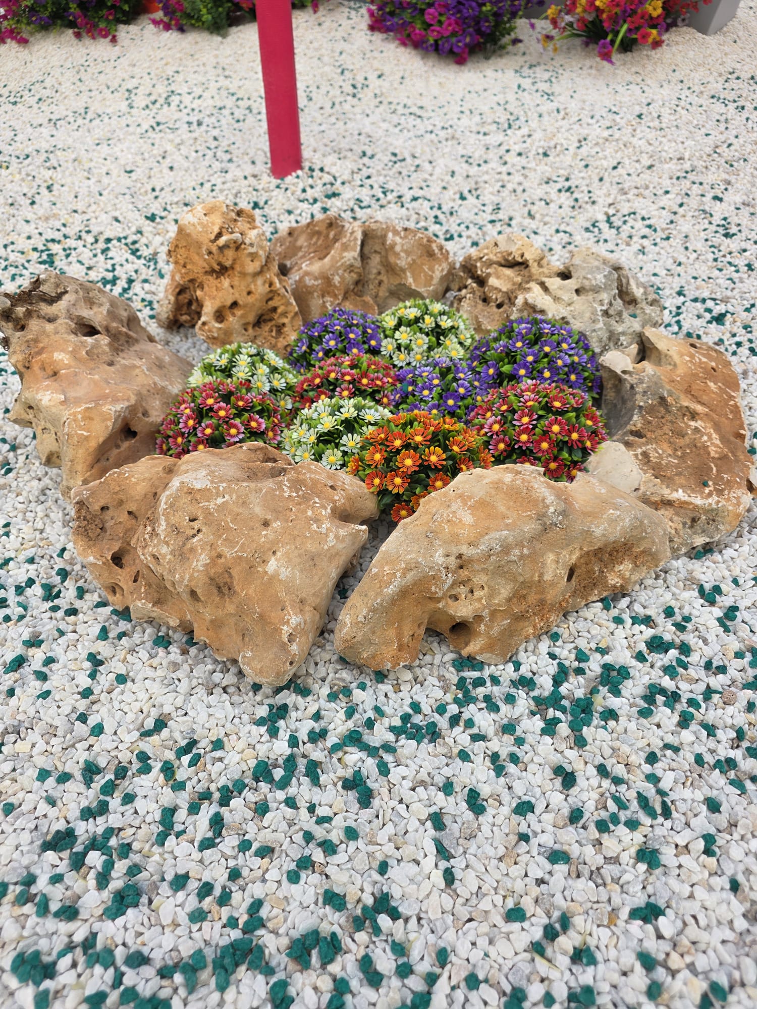 Detalle de la decoración de la Hoguera Grande Princesa Mercedes 2026, donde las plantas artificiales aportan color, volumen y un aspecto natural, integrándose con la piedra decorativa y la rocalla para completar la ambientación de la escena.